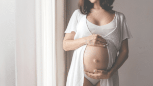Young Beautiful Pregnant Woman Standing near Window