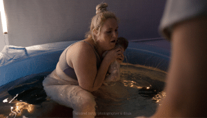 Mother catching her newborn baby during water birth