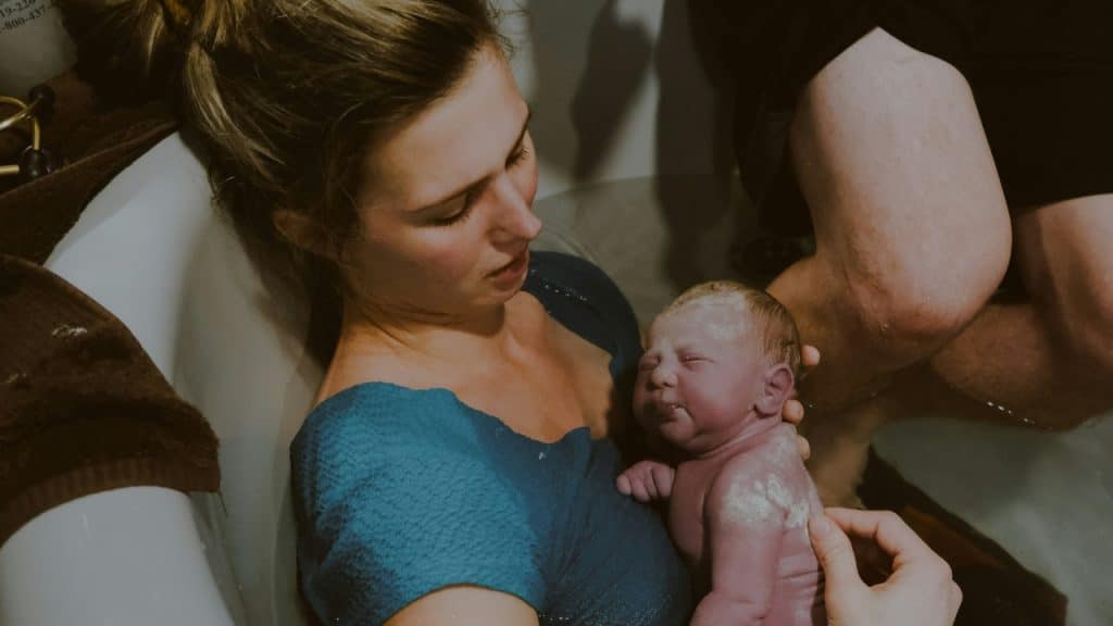 Mother, birth partner and baby in birth pool